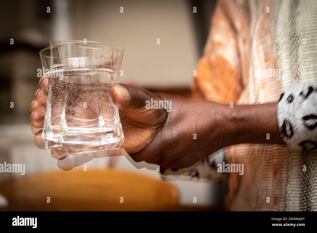 Doppia esposizione che crea un effetto sfocato in primo piano delle mani di una donna africana, mentre cerca di tenere costantemente un bicchiere. Concetto di difficoltà Foto Stock