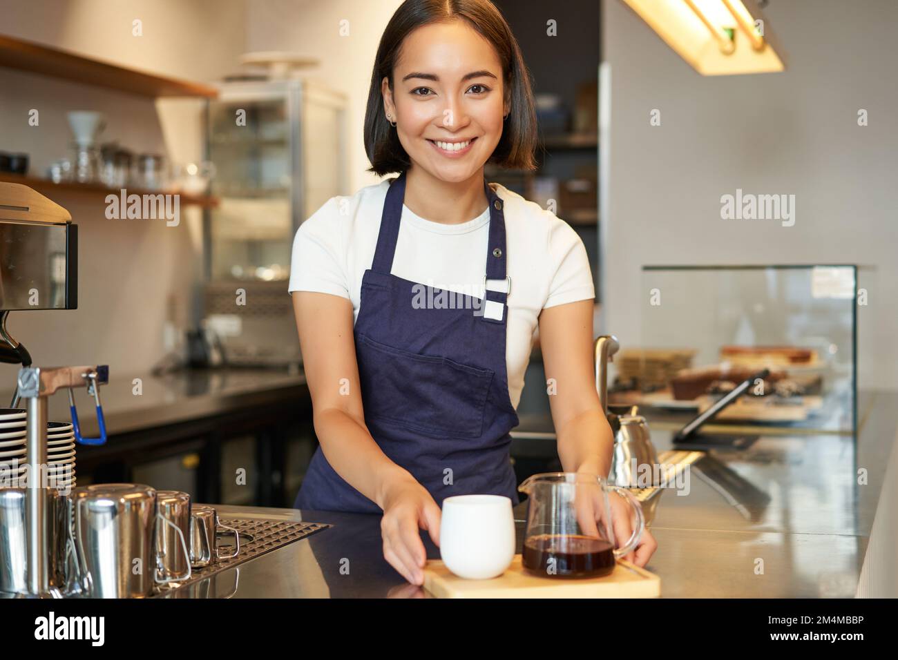 Sorridente bella barista ragazza in grembiule, preparare birra batch, caffè filtro, in piedi in caffè dietro il bancone Foto Stock