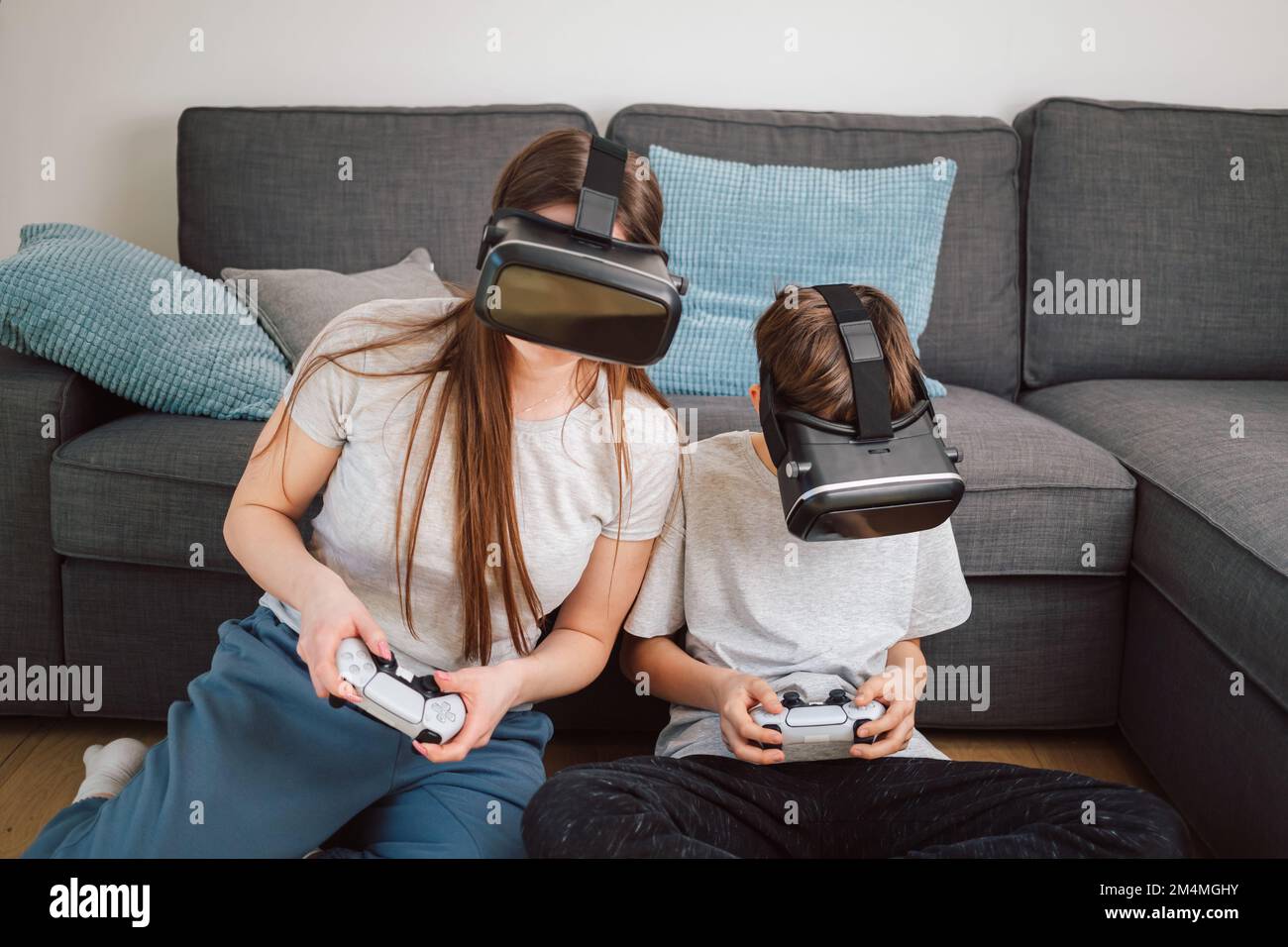 Madre e figlio amano giocare insieme con i videogame di intrattenimento, utilizzando gli occhiali e i controller VR seduti su un divano nel soggiorno Foto Stock