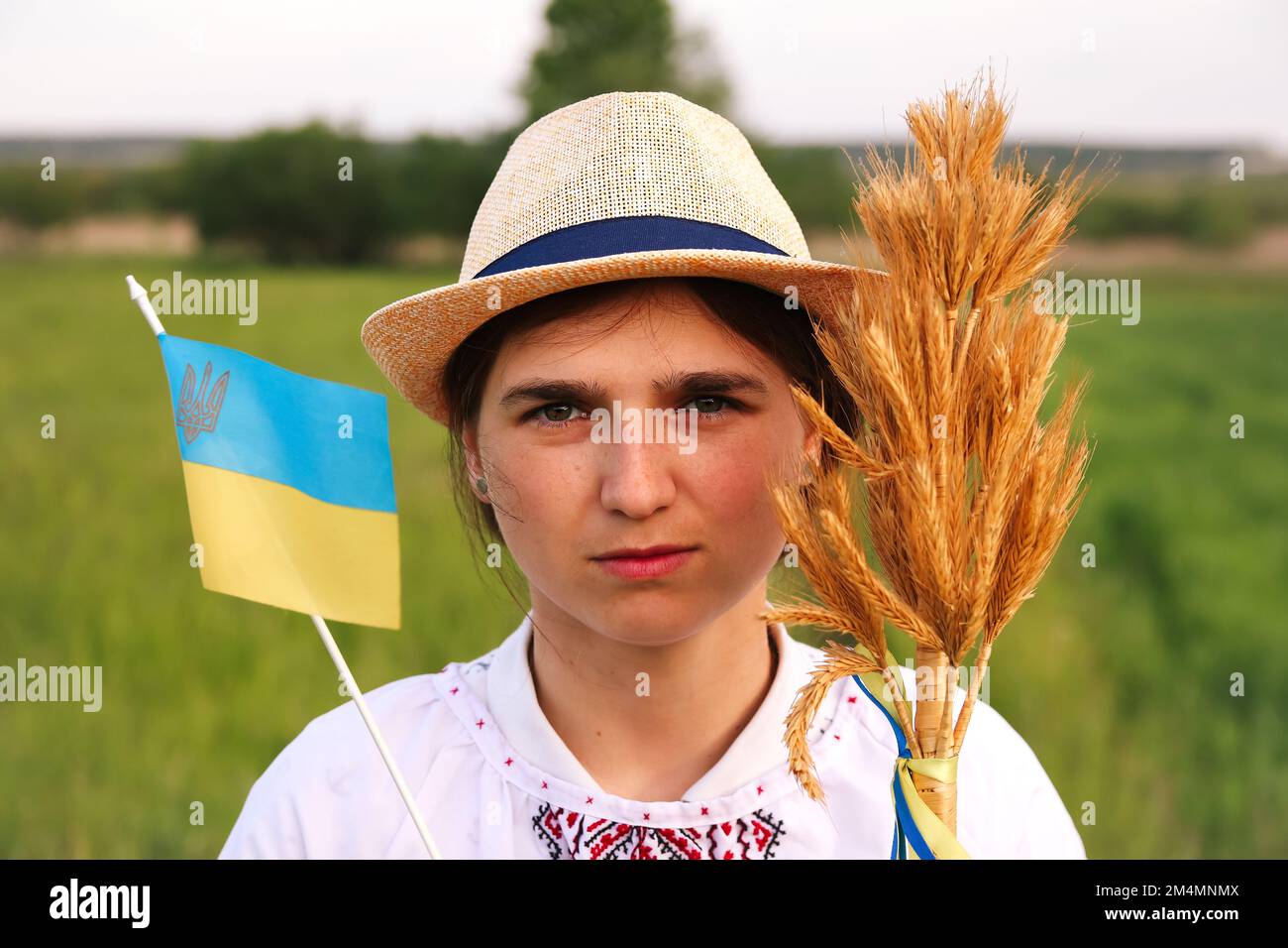Defocus giovane donna ucraina ritratto. Bouquet di spikelets d'oro maturi di grano legato sul prato natura sfondo. Bandiera Ucraina. Triste gi ucraino Foto Stock