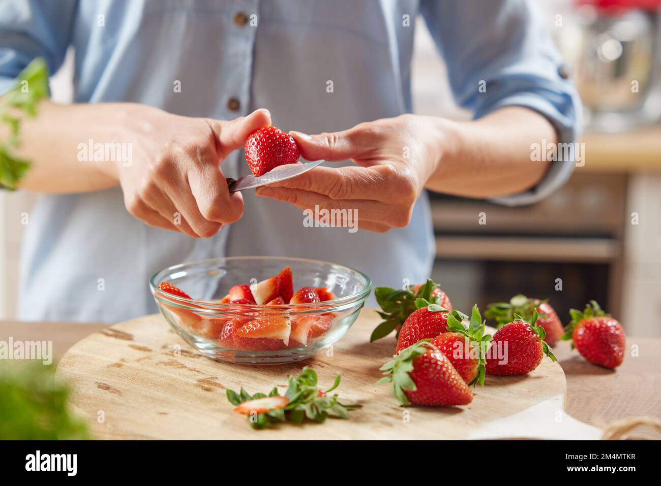 Ritaglia le anonime femmine che tagliano le fragole fresche in una ciotola di vetro mentre prepari una sana colazione in cucina a casa Foto Stock