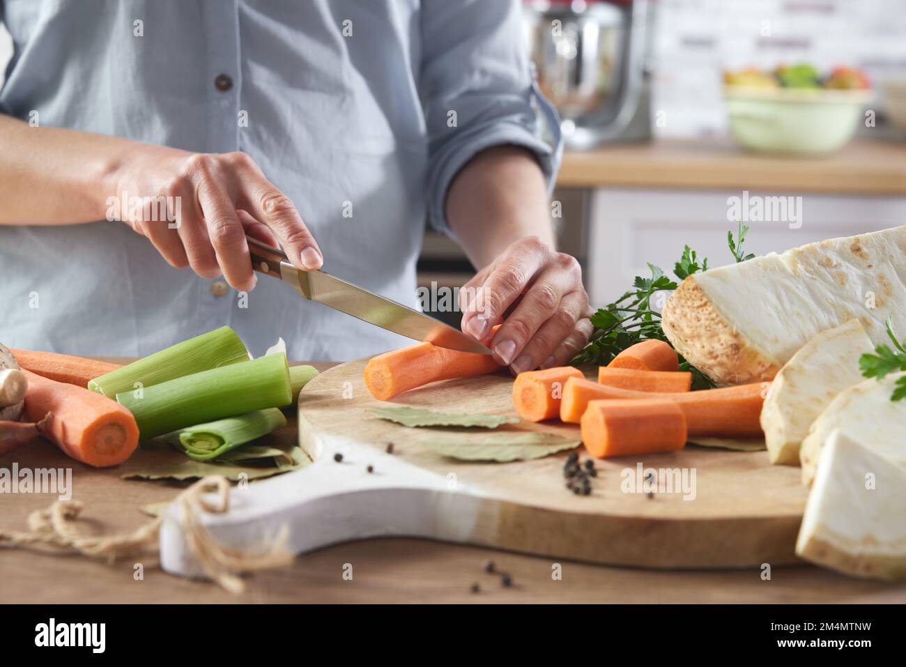 Crop anonimo femmina taglio carota fresca con coltello su tagliere di legno mentre preparando cibo sano in cucina a casa Foto Stock