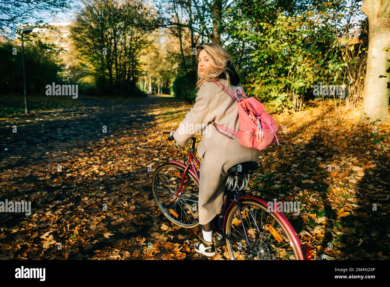 Giovane donna caucasica attraente cavalcare in bicicletta nel parco il giorno caldo in autunno. Foto Stock