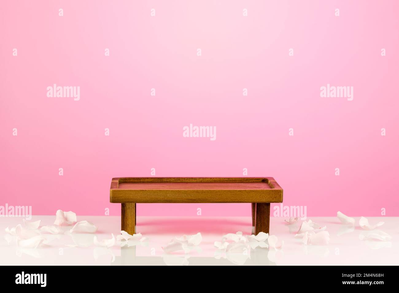 Podio vuoto in legno per alimenti, prodotti o cosmetici su sfondo a gradiente rosa con petali di rose. Piccolo tavolo decorativo per il montaggio del prodotto Foto Stock