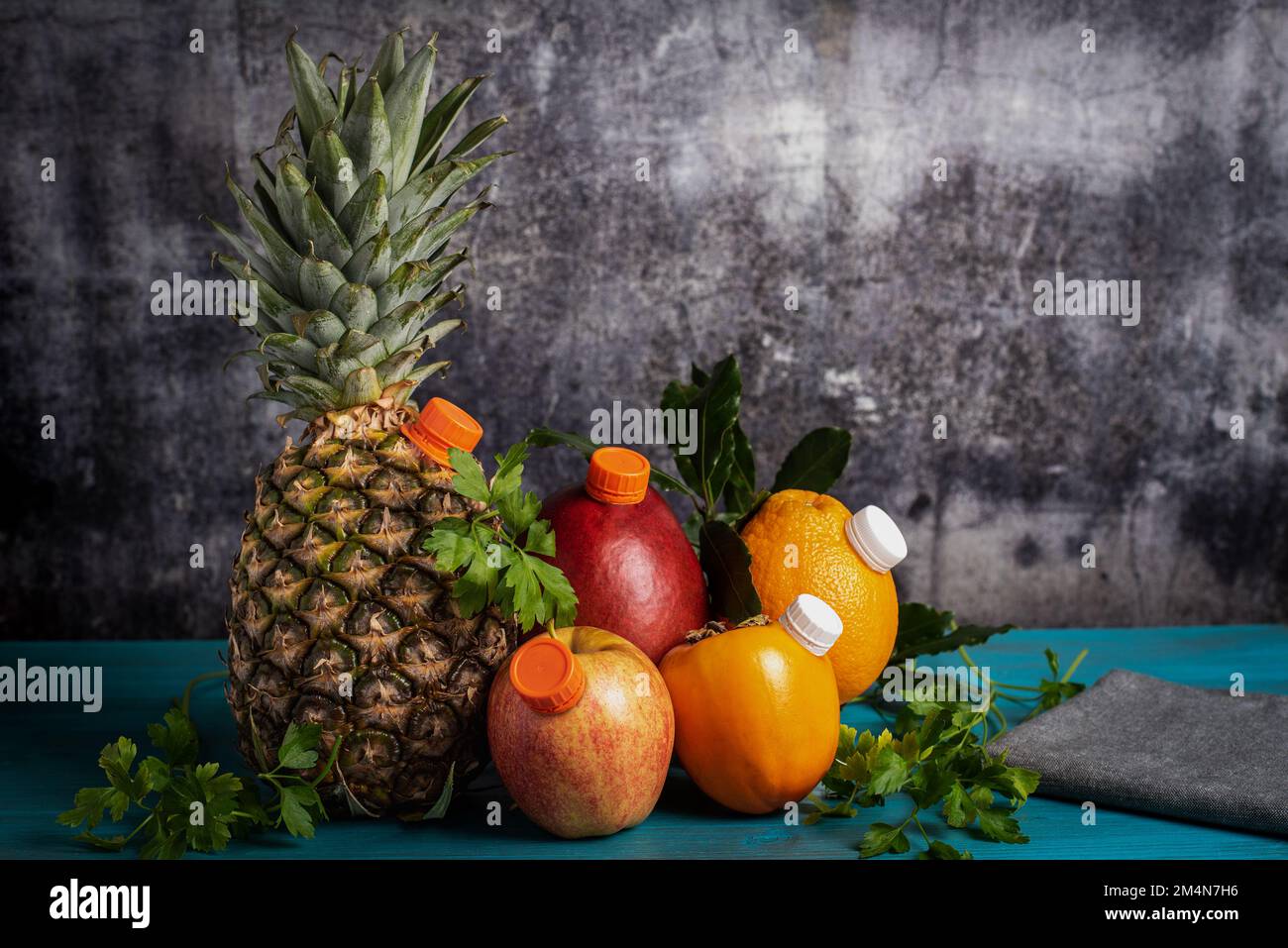 Ancora vita di frutta con beccucci come bottiglie di succo, con una base di legno blu e uno sfondo grigio parete. Foto Stock