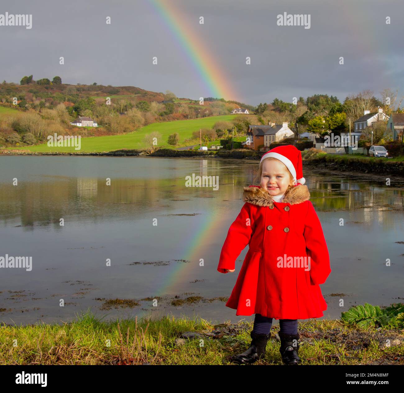 Giovane ragazza che indossa i panni di Natale in piedi di fronte a un arcobaleno. Foto Stock