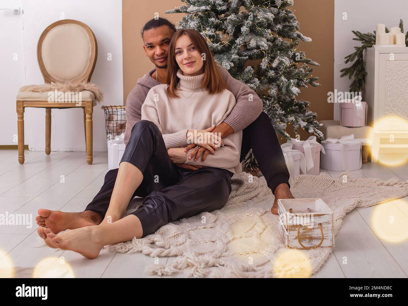Un ragazzo felice di stile in una felpa marrone è seduto abbracciando la sua ragazza, vicino all'albero di Natale Foto Stock