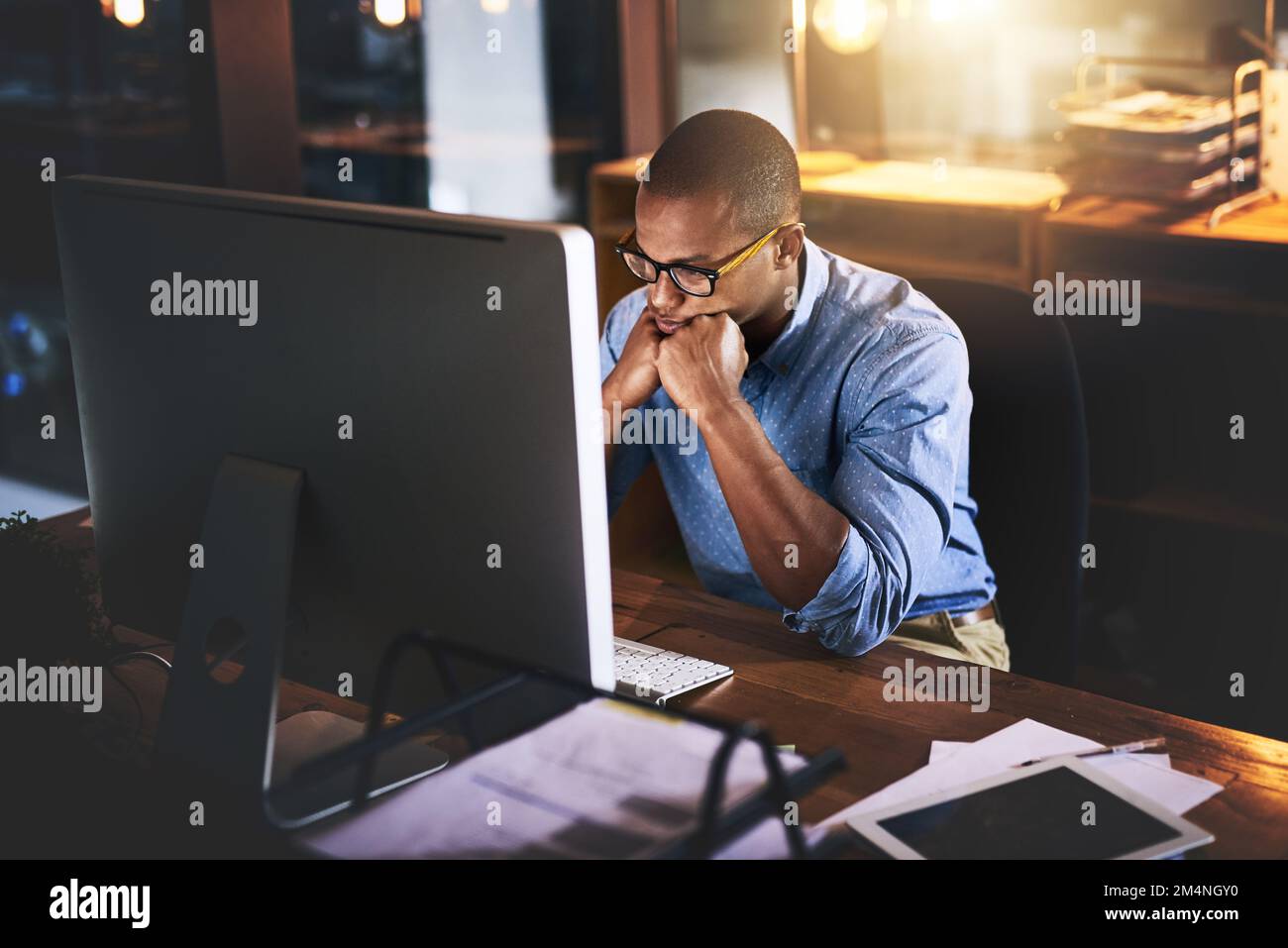 La dedizione non ha un tempo di bussare. un bel giovane uomo d'affari che usa un computer durante una tarda notte in un ufficio moderno. Foto Stock