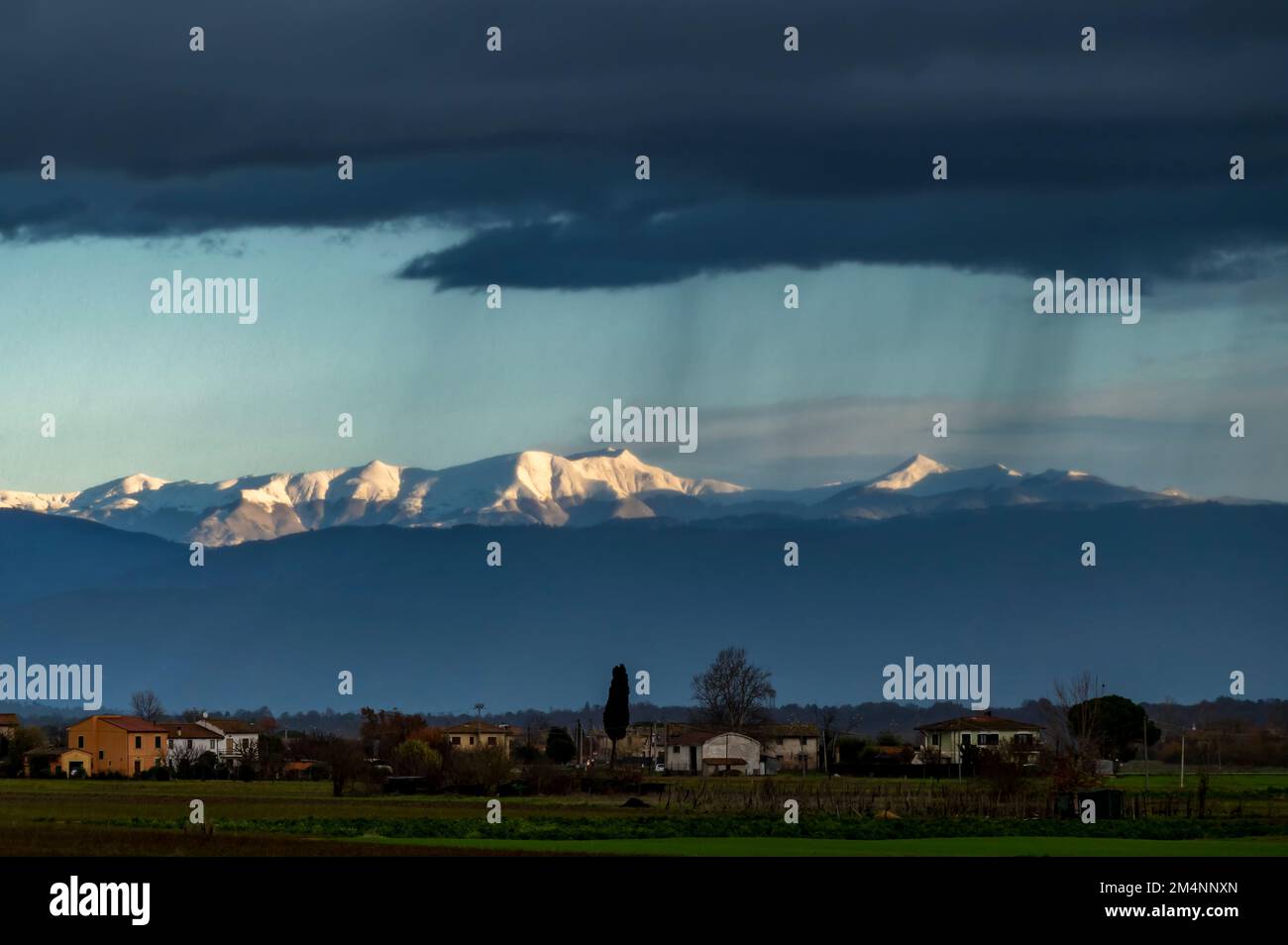 Nuvole nere e pioggia sulla campagna, con le montagne innevate sullo sfondo, Bientina, Pisa, Italia Foto Stock