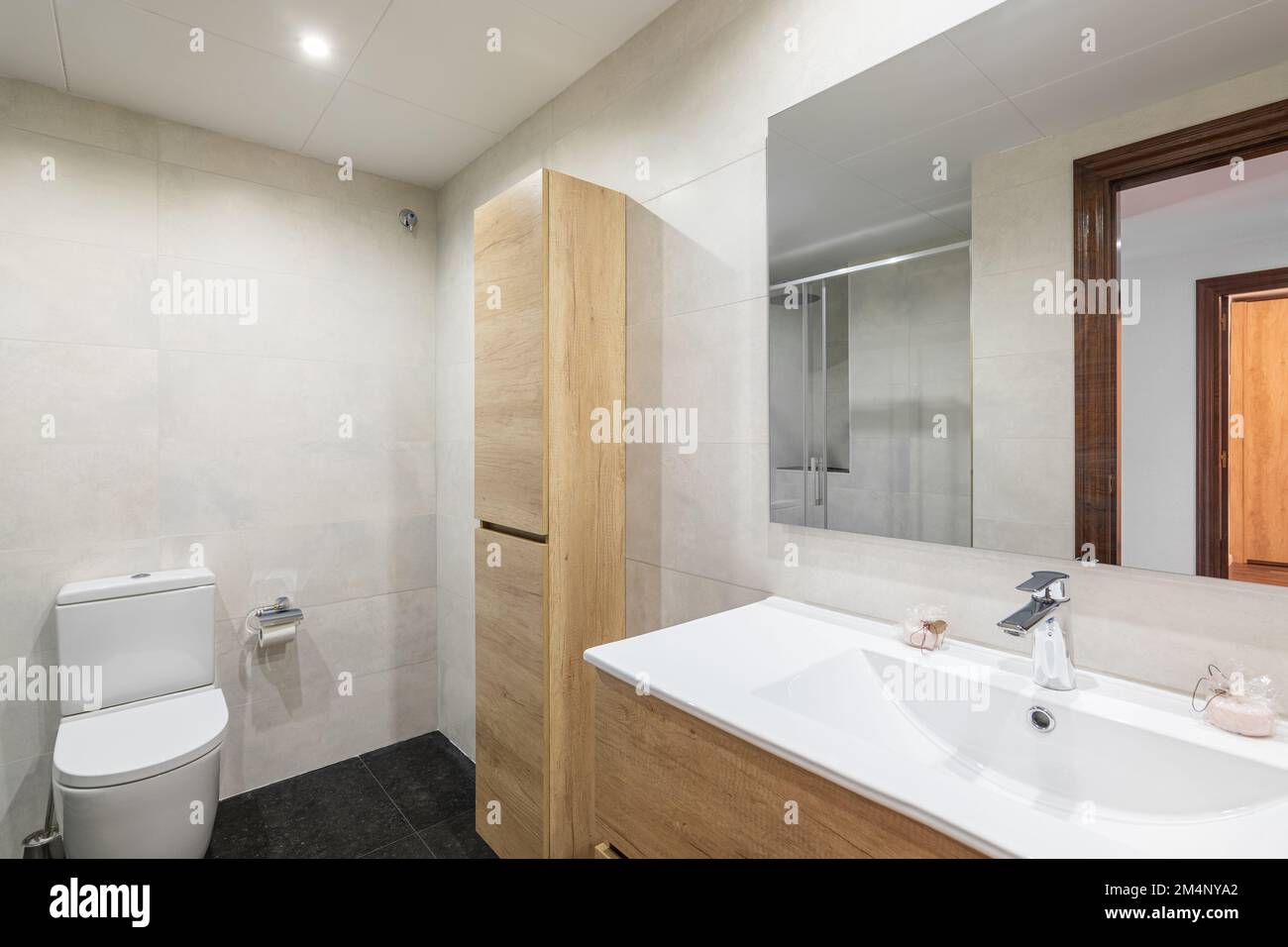 Bagno moderno con pareti piastrellate bianche. Piccolo armadio in legno per articoli da toeletta e asciugamani si appoggia contro la parete e si armonizza in colore con armadio per lavello Foto Stock