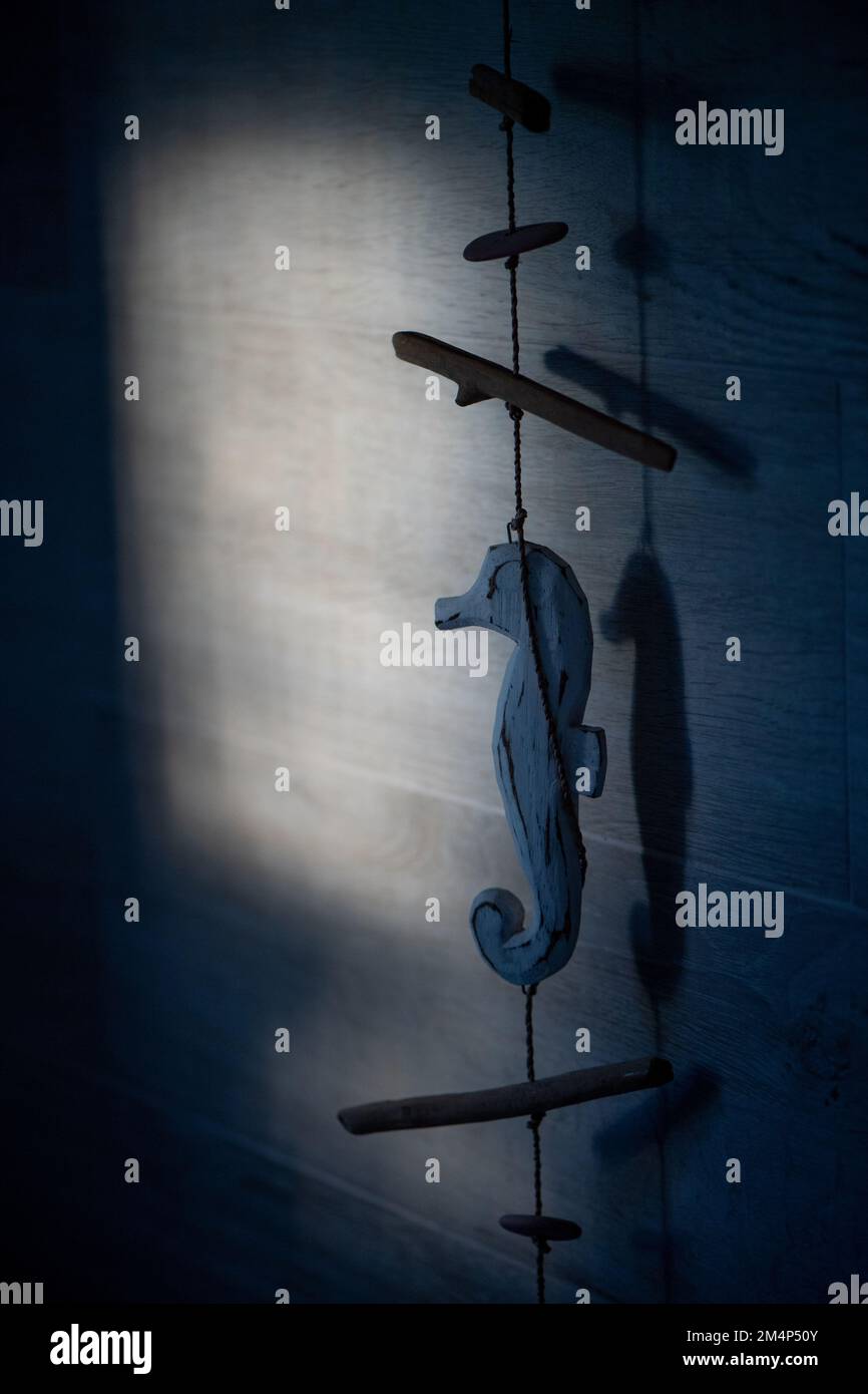 Splendida finestra che colpisce una parete del bagno piastrellata grigia con un ornamento di corda di legno di cavalluccio marino blu appeso con spazio copia. Foto Stock