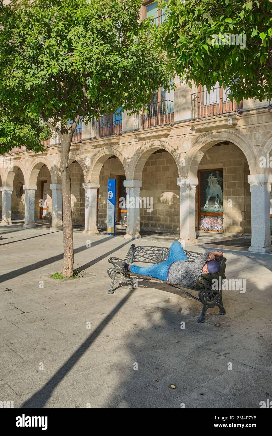 Persona che dorme su una panchina al sole in piazza Arenal a Jerez de la Frontera, Spagna Foto Stock