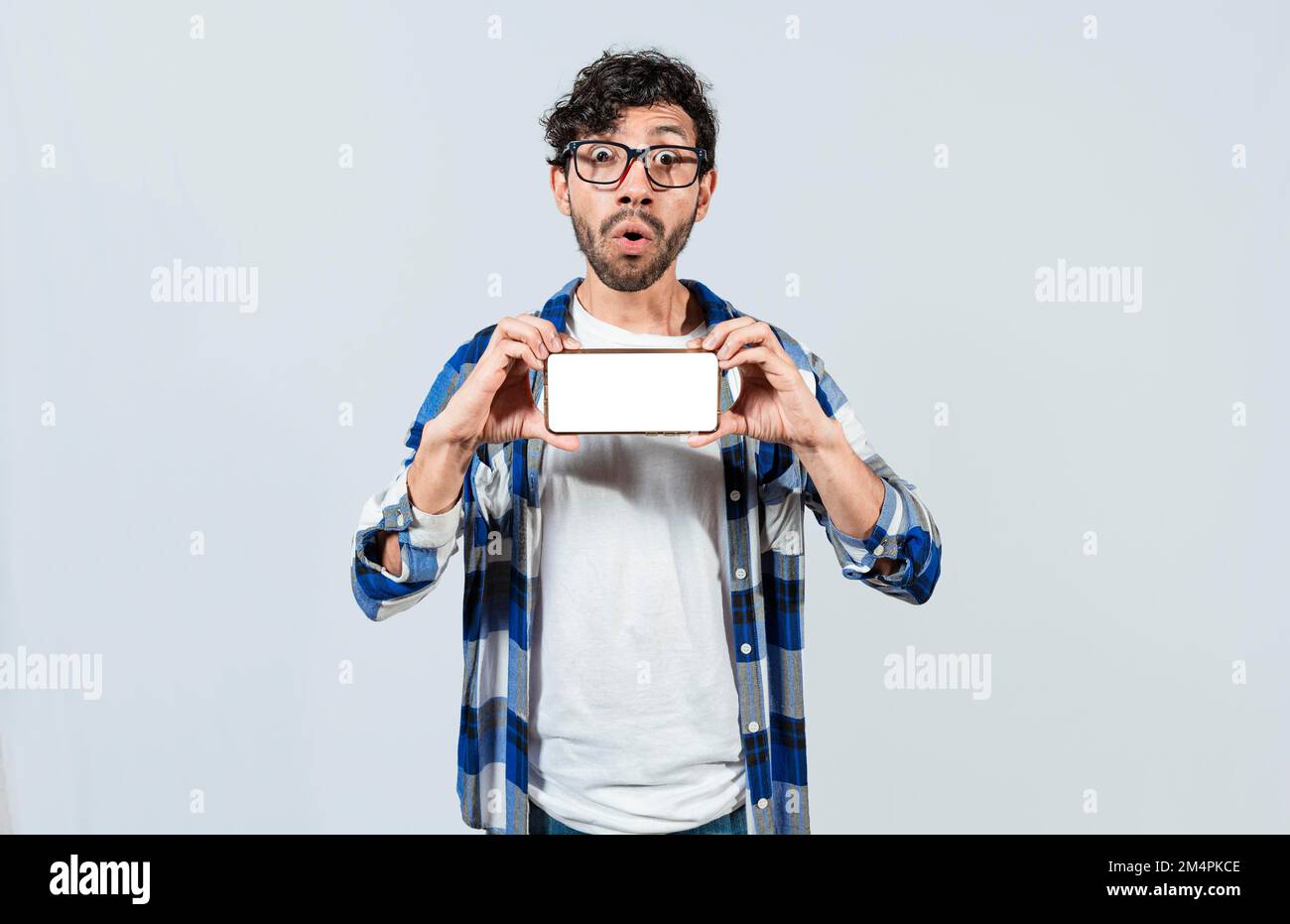 Un ragazzo sorpreso negli occhiali che mostra uno schermo vuoto dello smartphone. Stupito giovane uomo che mostra annuncio sul cellulare. Stupito bell'uomo che mostra l'orizzontale Foto Stock