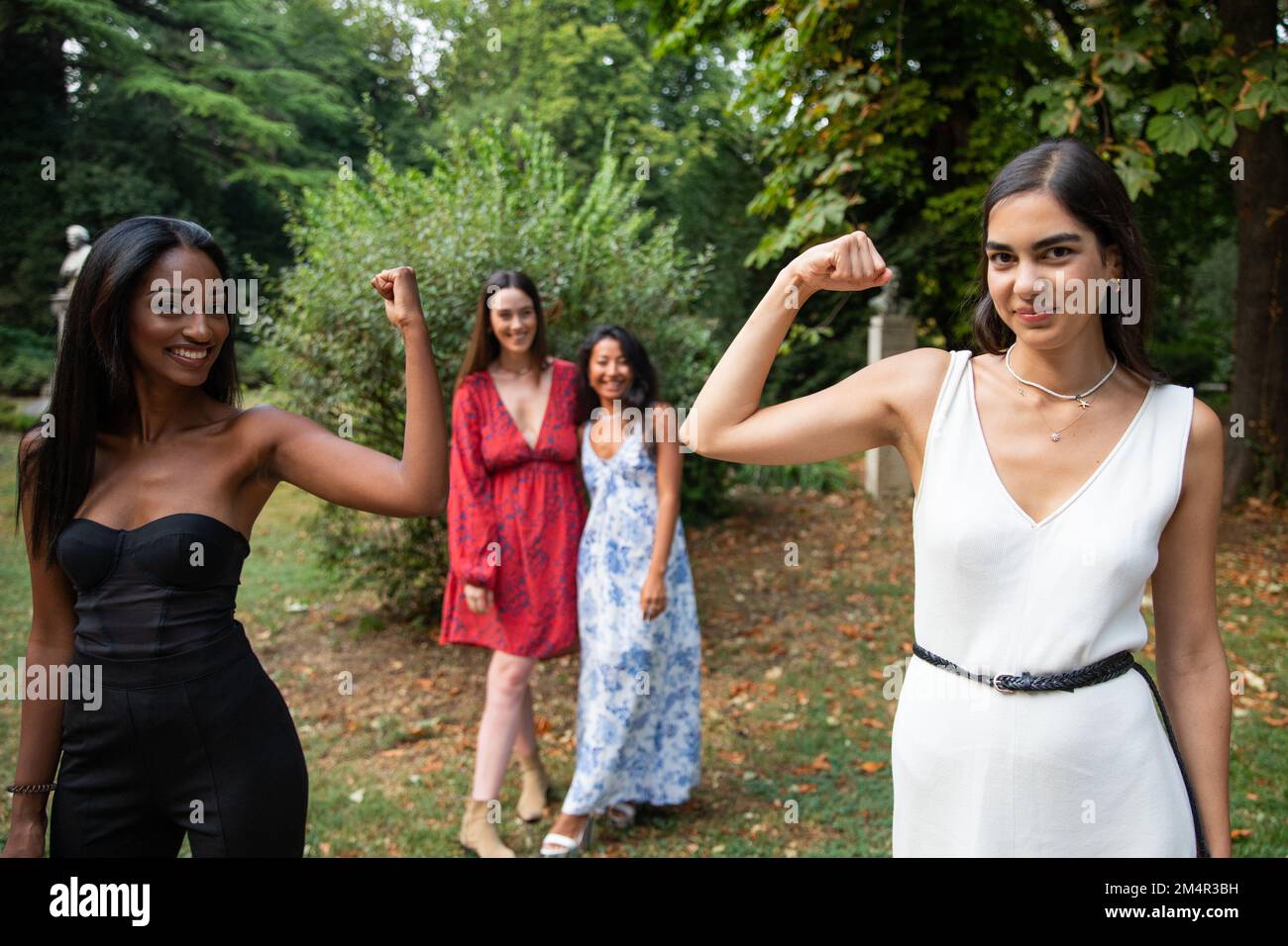 Due amici femminili mostrano bicipiti con due amici femminili dietro guardarli, concetto di empowerment femminile Foto Stock