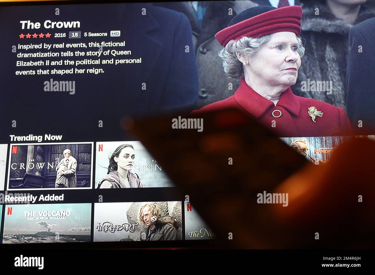 Applicazione Netflix sullo schermo tv evidenziando il programma televisivo Netflix The Crown con l'ombra di qualcuno che tiene un telecomando TV davanti. Foto Stock
