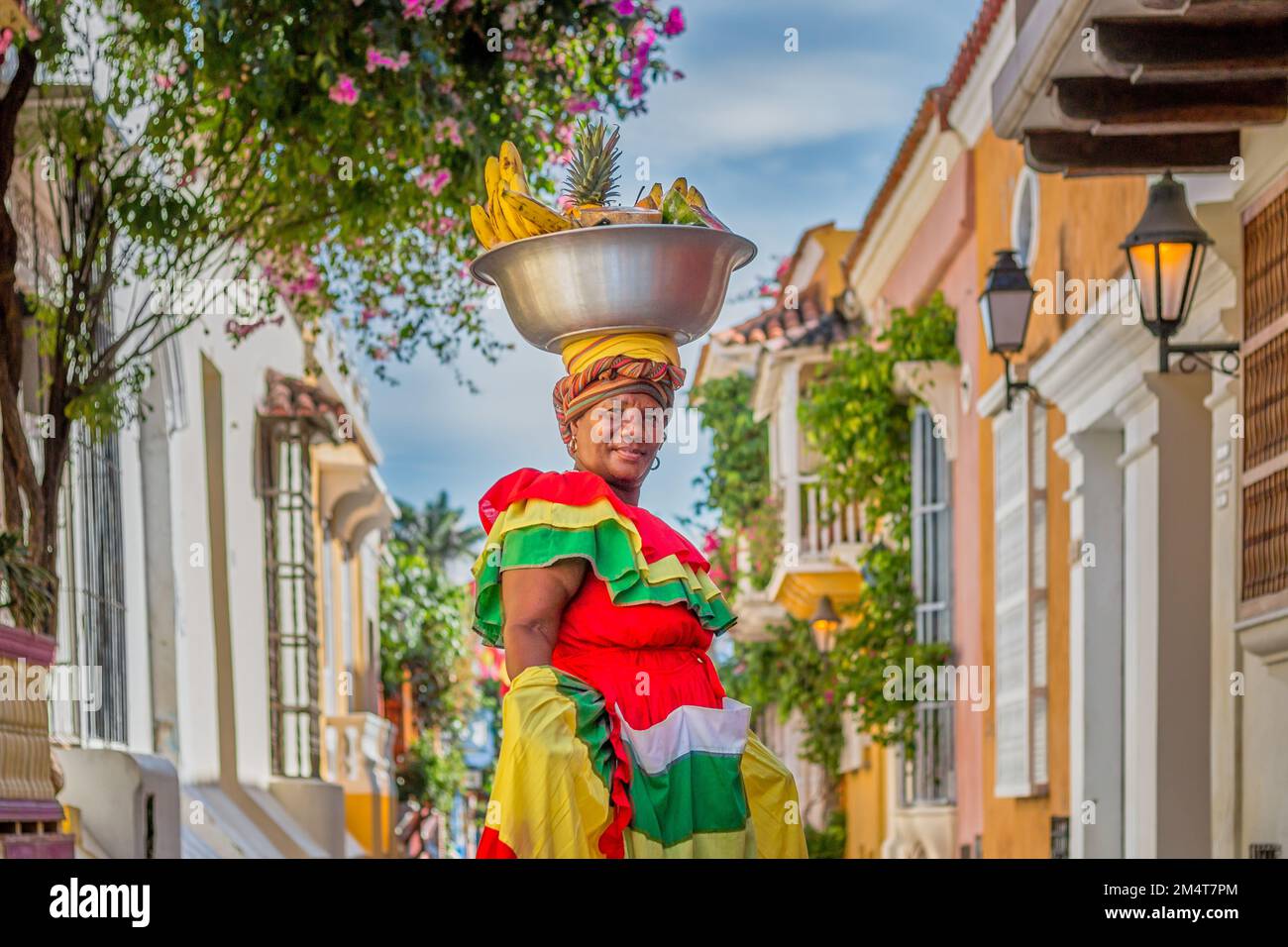 Un filmato regolare di un Palenquera che tiene una grande ciotola di frutta in testa, vestita con abiti colorati in una strada a Cartagena, Spagna Foto Stock