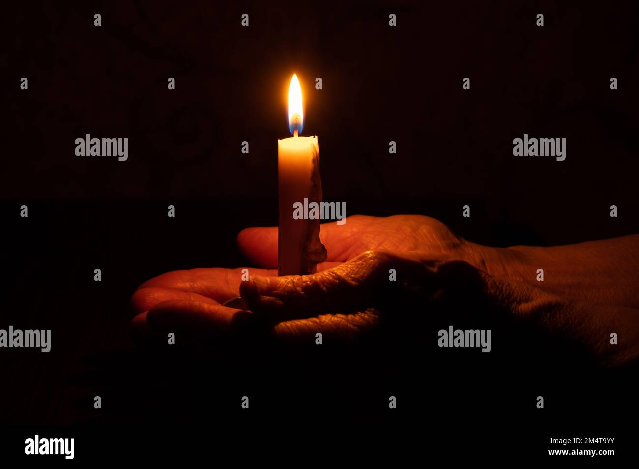 le mani della vecchia donna e la fiamma della candela al buio, la luce della candela, il lutto, la candela al buio Foto Stock