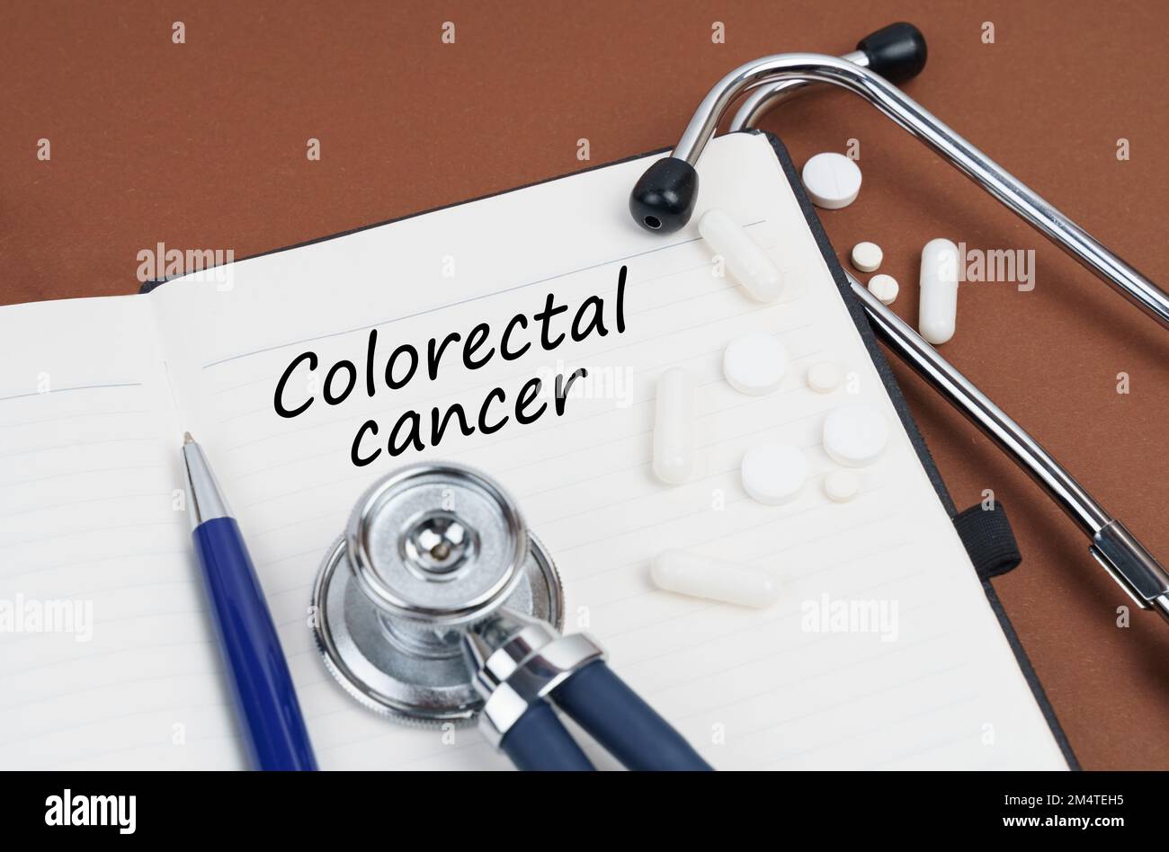 Medicina e concetto di salute. Su una superficie marrone si trovano pillole, una penna, uno stetoscopio e un notebook con l'iscrizione - cancro colorettale Foto Stock