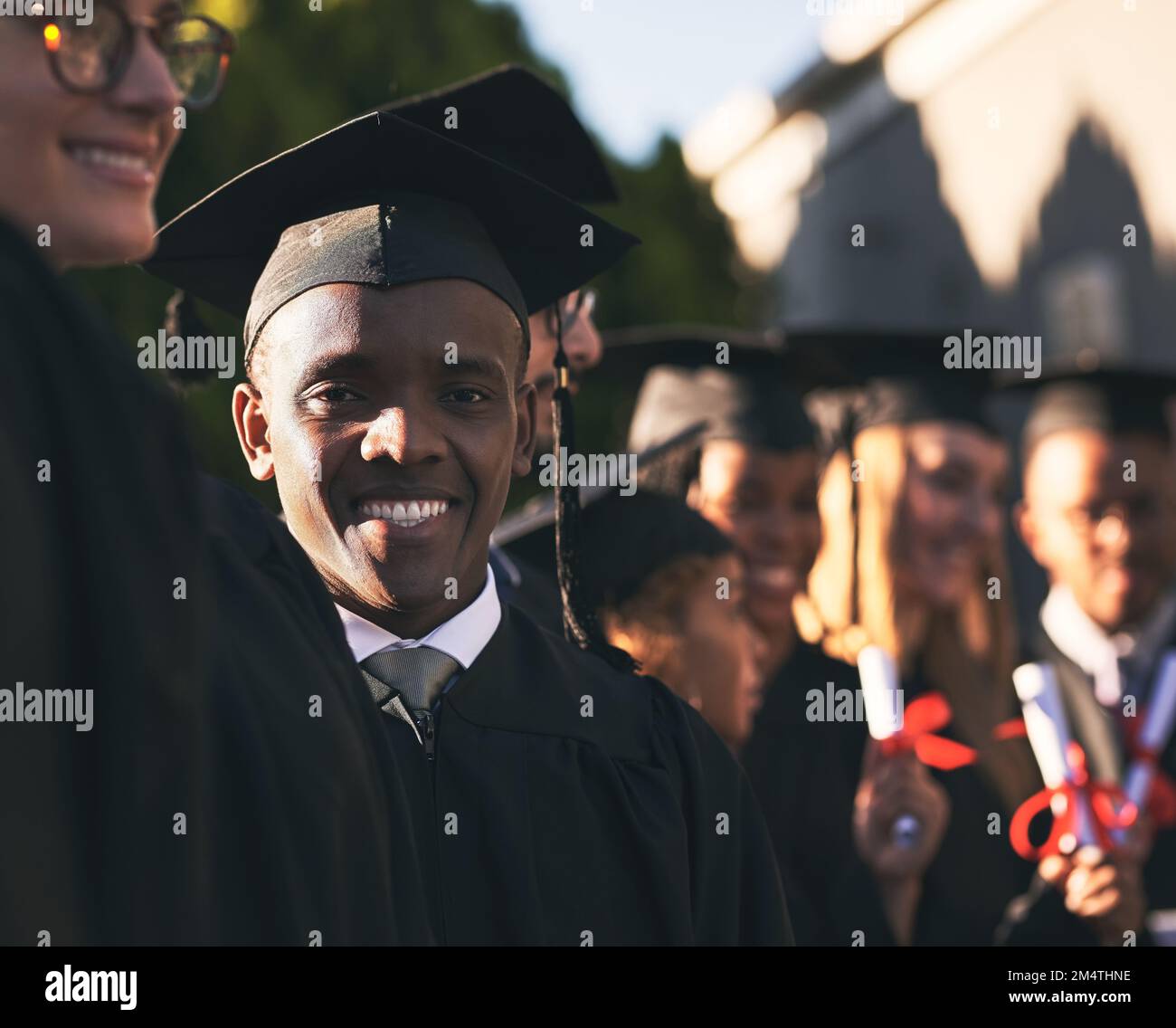 Quegli anni ne sono valsa la pena. Ritratto di uno studente universitario sorridente il giorno della laurea con i compagni di classe sullo sfondo. Foto Stock