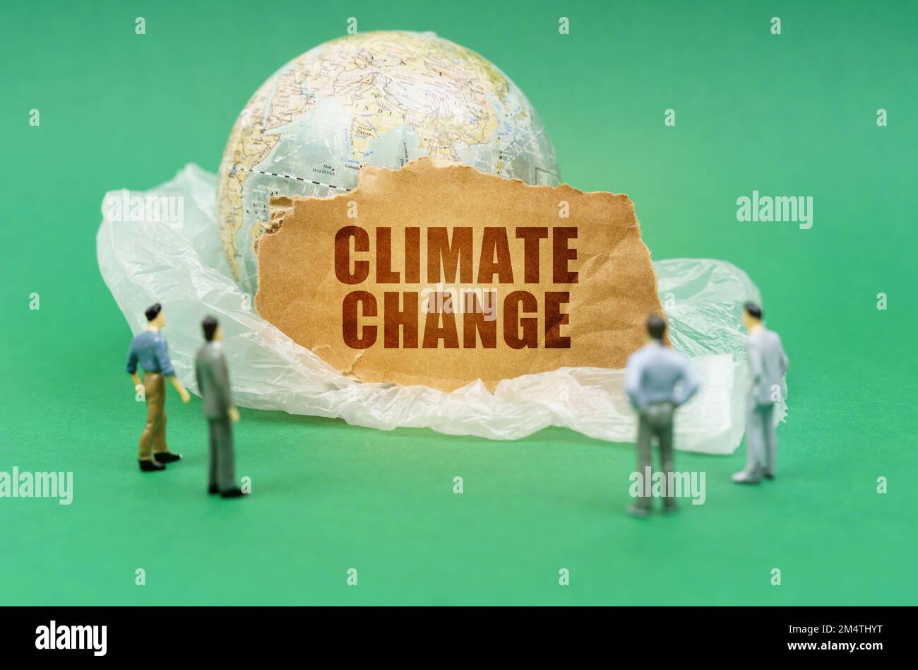 Concetto ecologico. Su uno sfondo verde su un sacchetto di plastica è un globo e un segno con l'iscrizione - cambiamento climatico. Cifre quasi sfocate di p Foto Stock