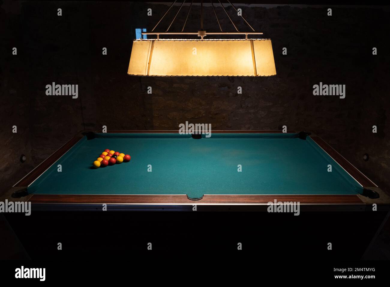 Un filmato regolare di un tavolo da biliardo in una stanza buia con palline colorate su di esso e una lampada sopra Foto Stock