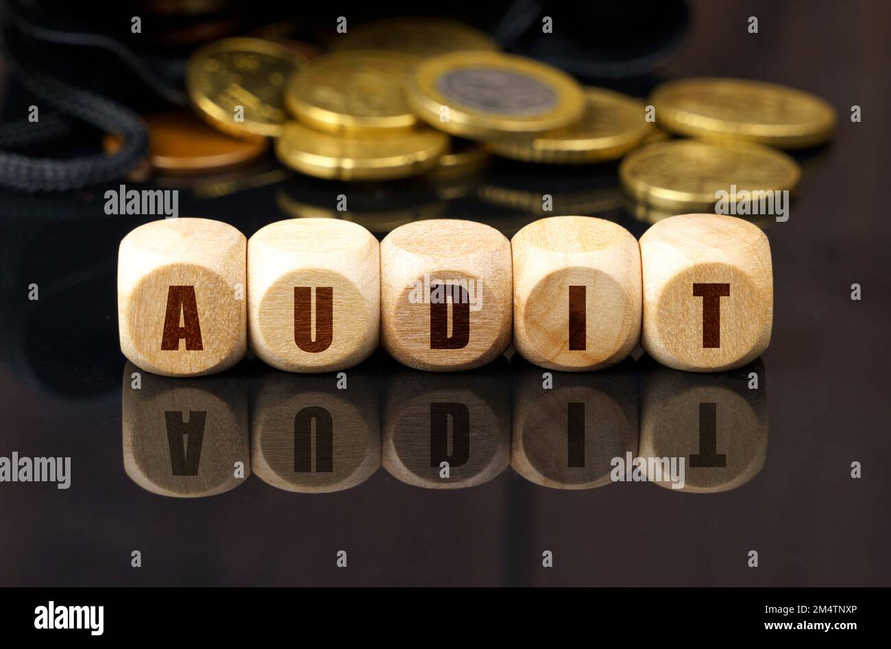 Business e concetto di economia. Su una superficie nera riflettente sono le monete e i cubi di legno con l'iscrizione - AUDIT Foto Stock