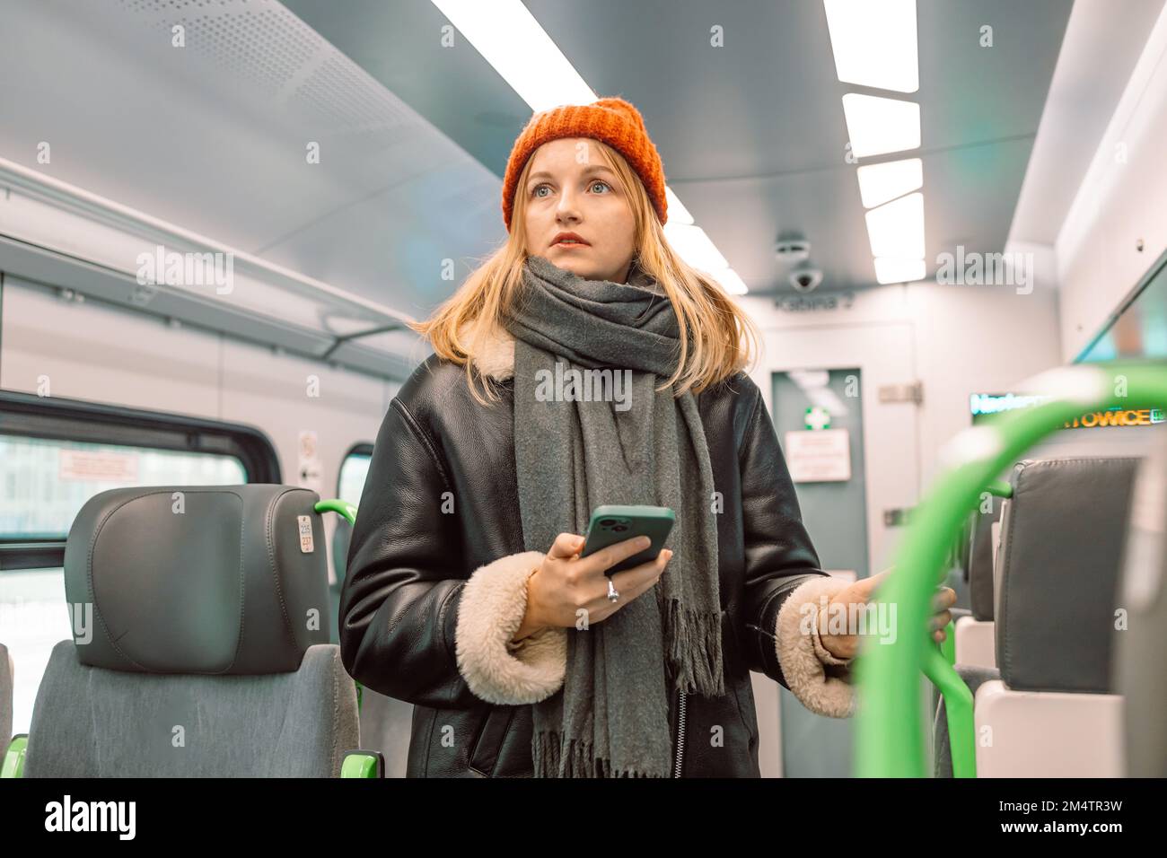 Triste ragazza bionda con uno smartphone si è persa cercando il suo posto in un treno veloce ad alta velocità Foto Stock