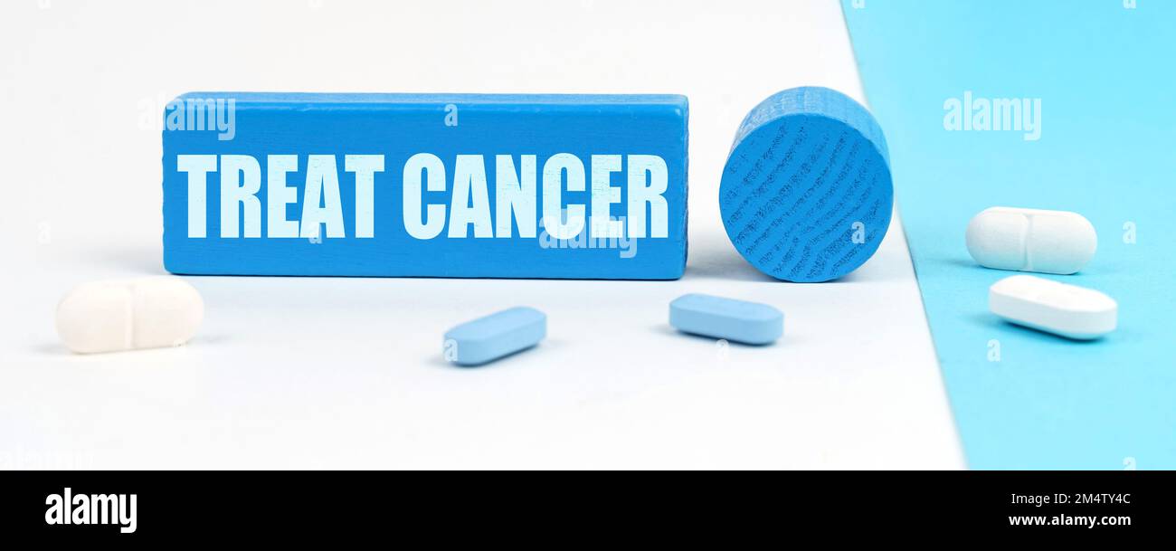 Concetto medico. Su una superficie bianca e blu ci sono pillole, uno stetoscopio, una penna e un segno di legno con l'iscrizione - Treat Cancer Foto Stock