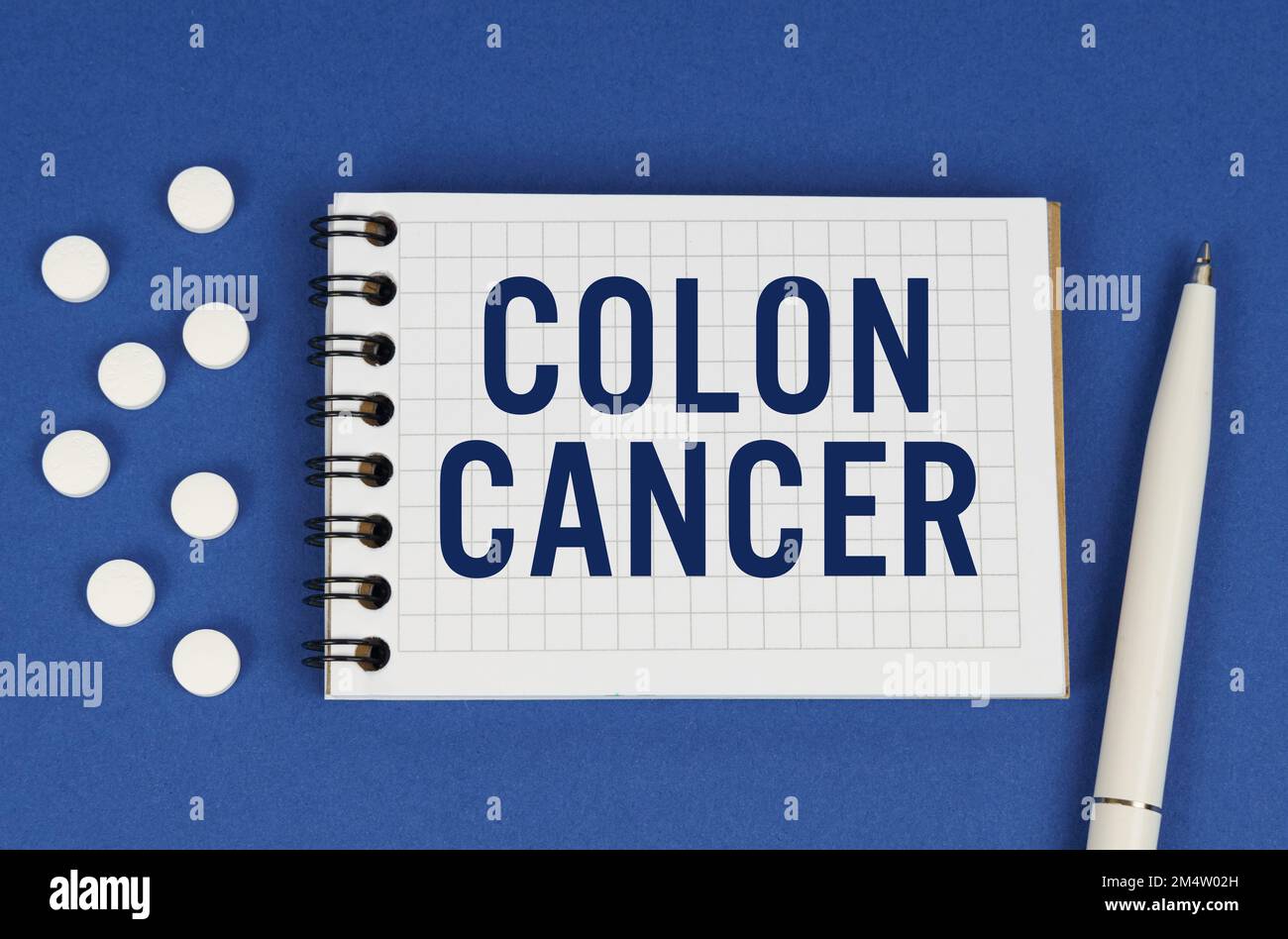 Concetto medico. Su uno sfondo blu, una penna, compresse e un blocco note con l'iscrizione - CANCRO DEL COLON Foto Stock