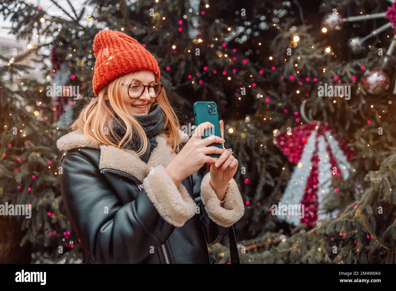 Shopping, vacanze invernali e concetto di persone. Felice donna bionda scatta una foto di un mercatino di Natale europeo con uno smartphone. Festeggiamo il nuovo Foto Stock
