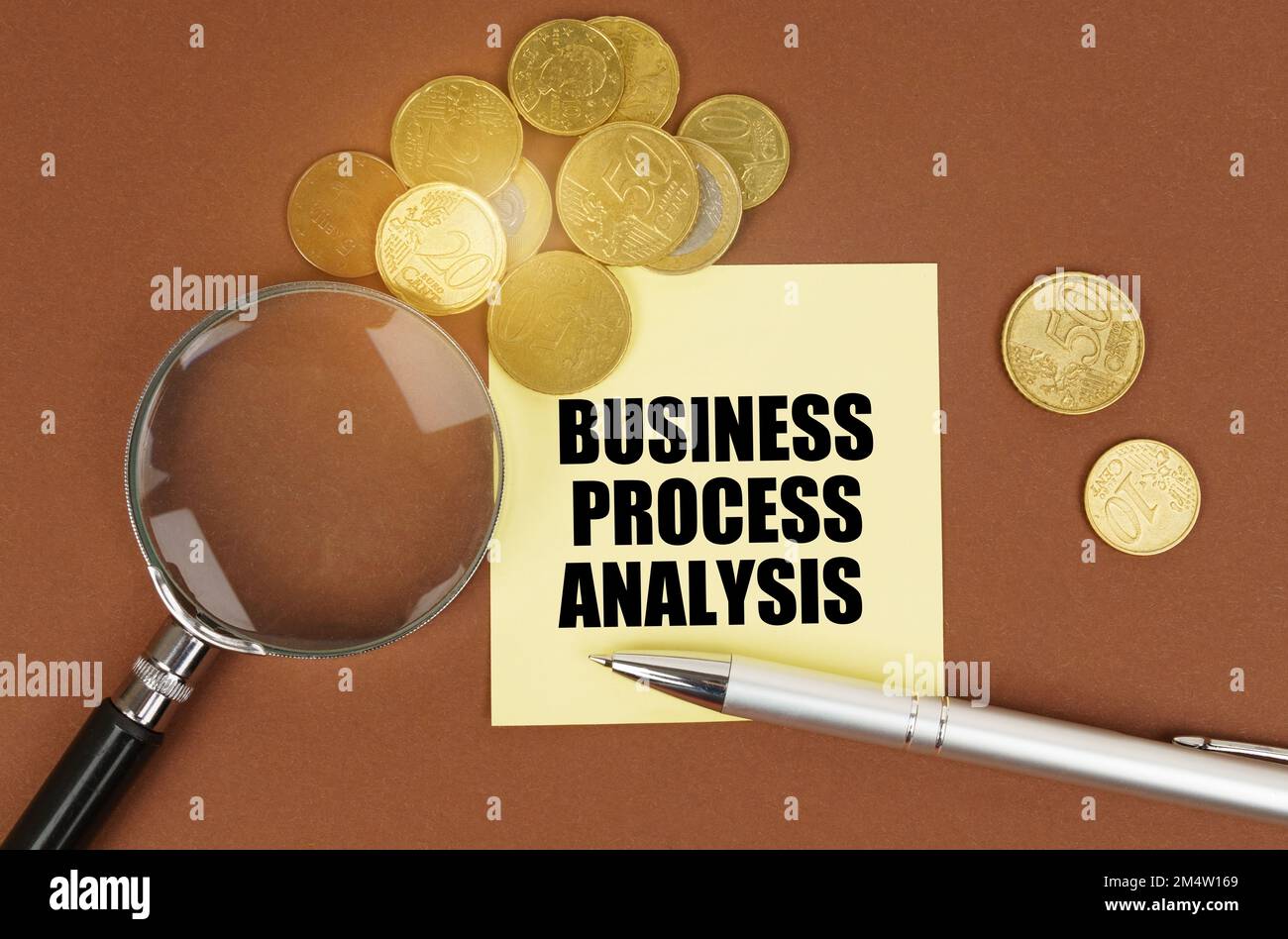Concetto aziendale. Su una superficie marrone ci sono monete, una penna, una lente d'ingrandimento e adesivi con l'iscrizione - ANALISI DEL PROCESSO AZIENDALE Foto Stock