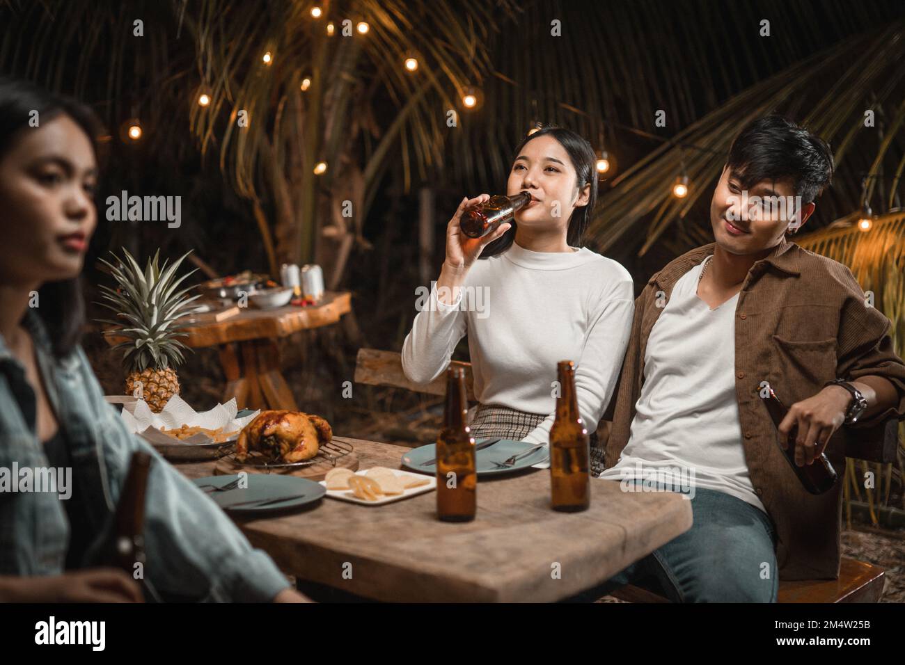 Donna che tiene una bottiglia di birra bere a una festa e il giovane uomo gesti flirtatiously Foto Stock