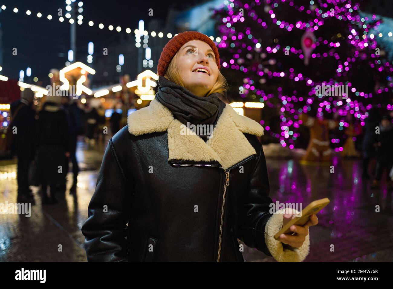 Donna che utilizza lo smartphone sul mercato di Natale europeo. Ragazza che si diverti durante le festività invernali, utilizzando il telefono, i social network, le comunicazioni e l'app Foto Stock