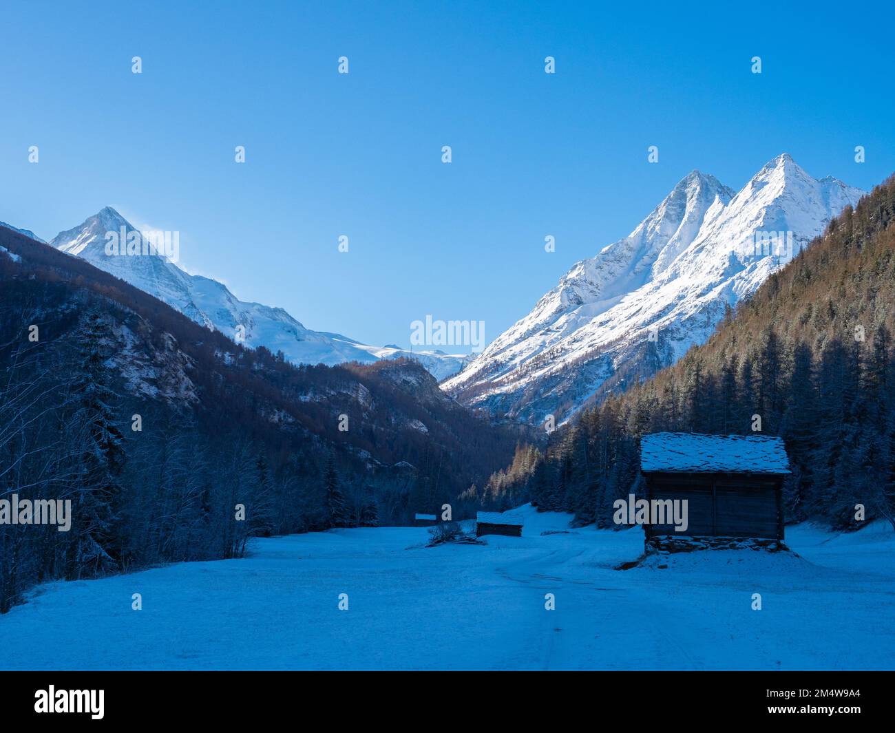 Val d'Herens, Svizzera - Aprile 10th 2022: Vista invernale mattutina da una valle all'ombra verso le cime alpine illuminate dal sole Foto Stock