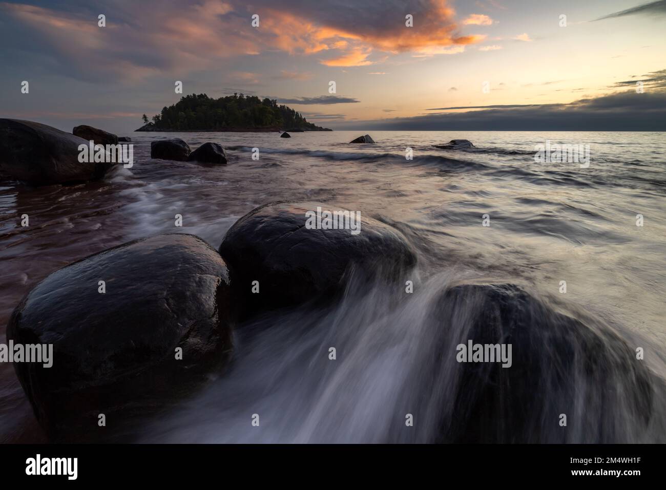 Le onde si riversano intorno alle rocce costiere mentre il sole sorge sul lago Superior a Little Presque Isle Park vicino a Marquette Michigan, USA Foto Stock