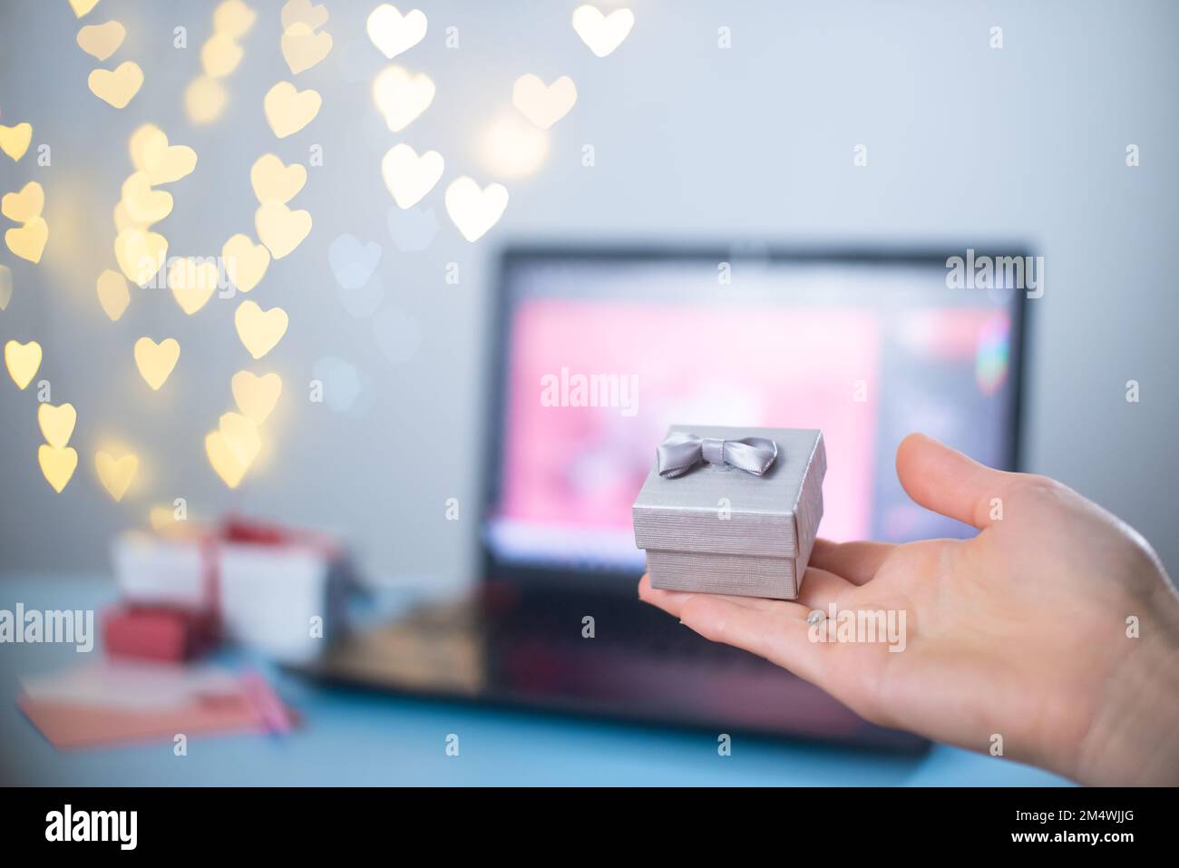 Regalo di San Valentino in una piccola scatola, shopping online, ricerca sul laptop per un regalo. Dichiarazione d'amore. Bokeh e regali di Natale sullo sfondo. Foto Stock