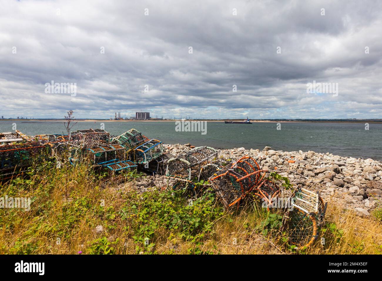 Una vista di Teesport da South Gare, Redcar, Inghilterra, Regno Unito con le creelle di aragosta in primo piano e centrale elettrica e draga in background Foto Stock