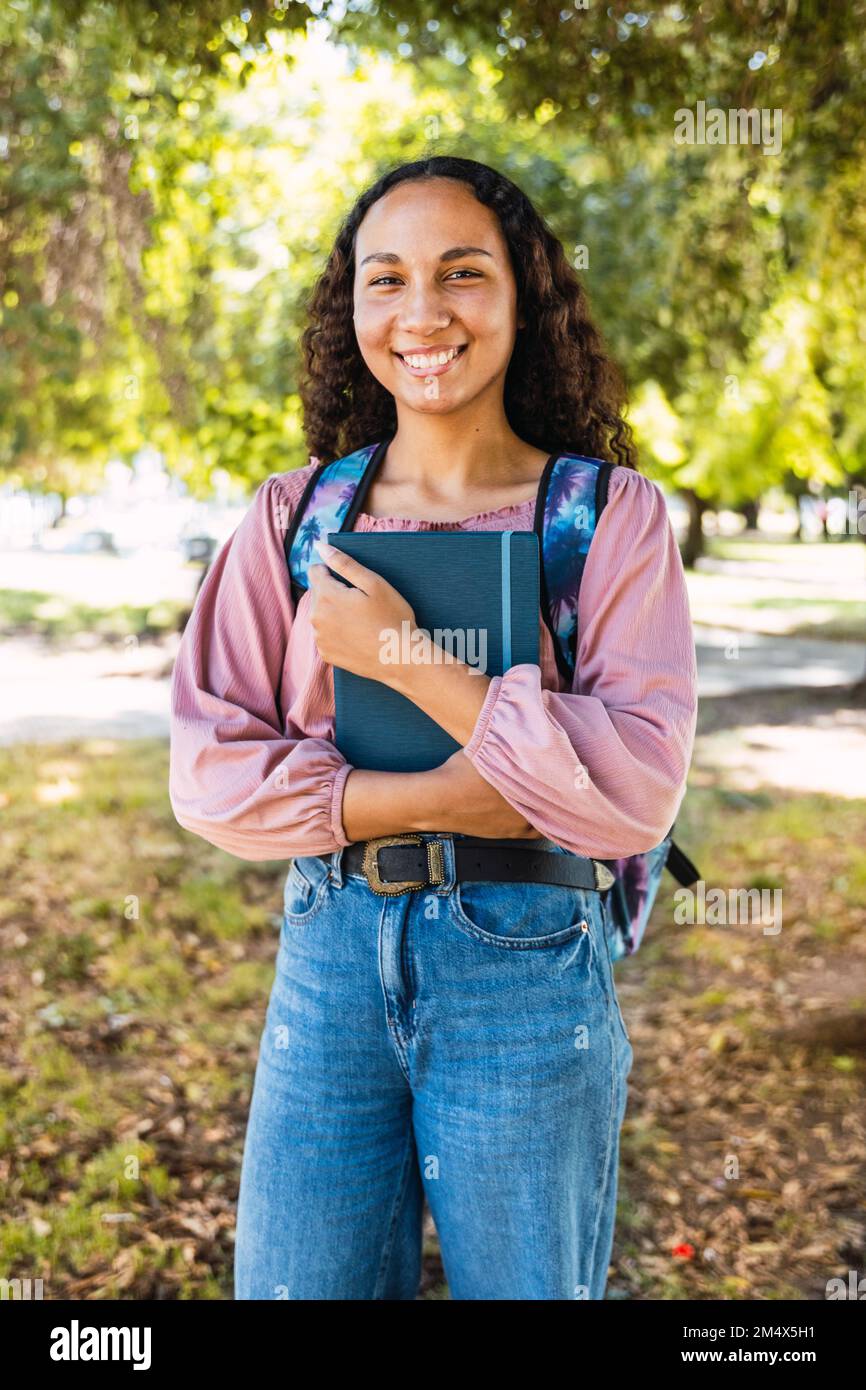 Primo piano felice giovane studentessa latina che tiene i suoi libri nel parco. Fiducia in se stessi Foto Stock