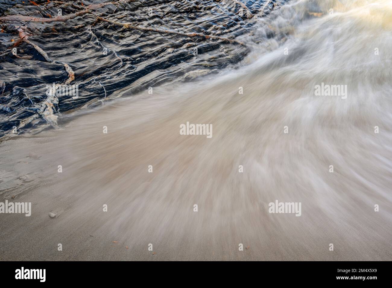 Onde entranti, sabbia bagnata e un affioramento roccioso con intrusioni ignee, Lake Superior Provincial Park- Coldwater River Bay, Ontario, Canada Foto Stock