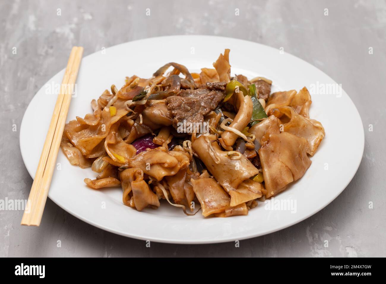 Spaghetti fritti con verdure e manzo in piatto bianco su rosa Foto Stock