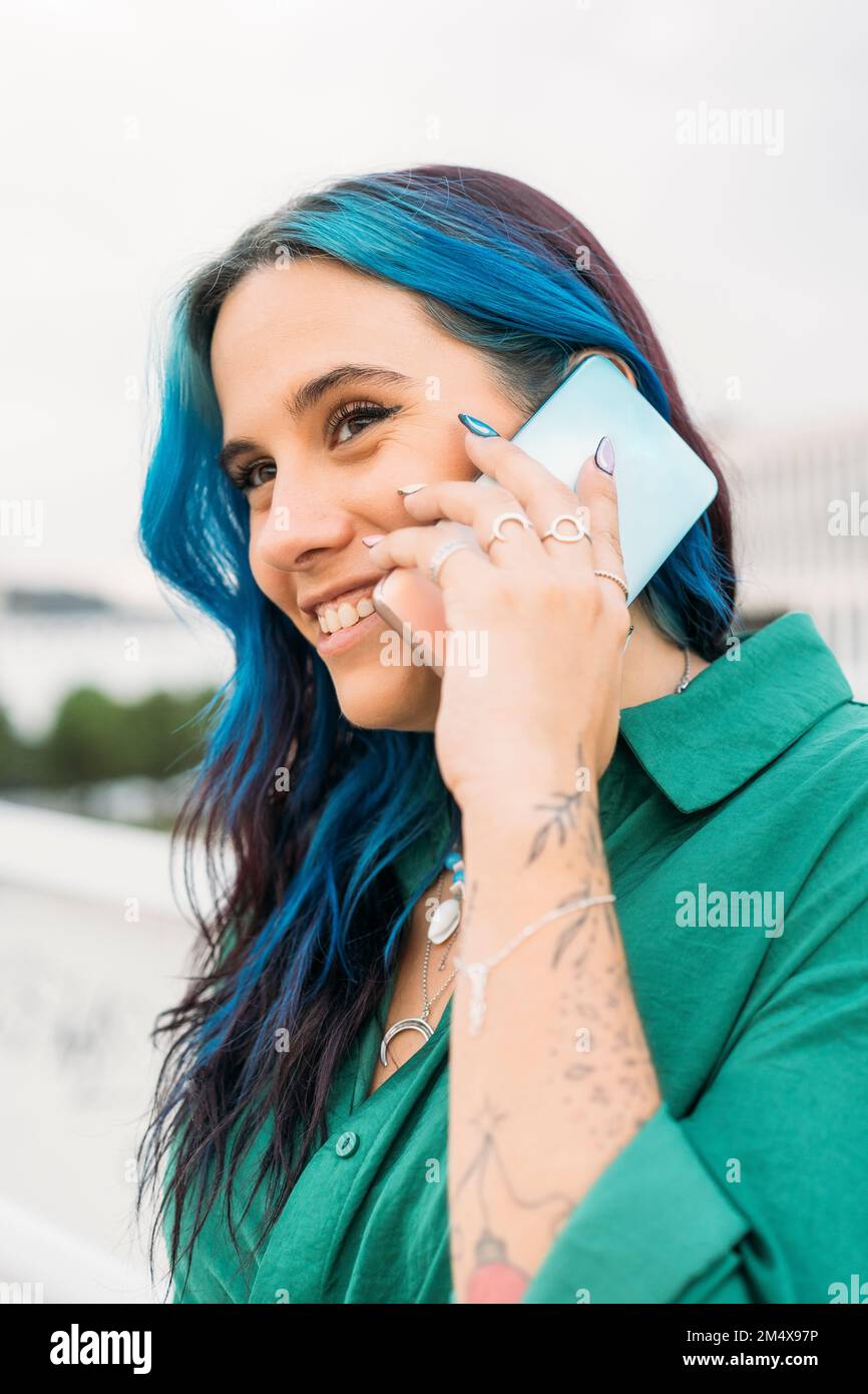 Donna con i capelli evidenziati blu che parlano sullo smartphone Foto Stock