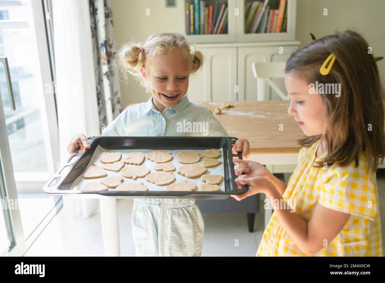 Ragazza felice con un amico che tiene il vassoio dei biscotti a casa Foto Stock