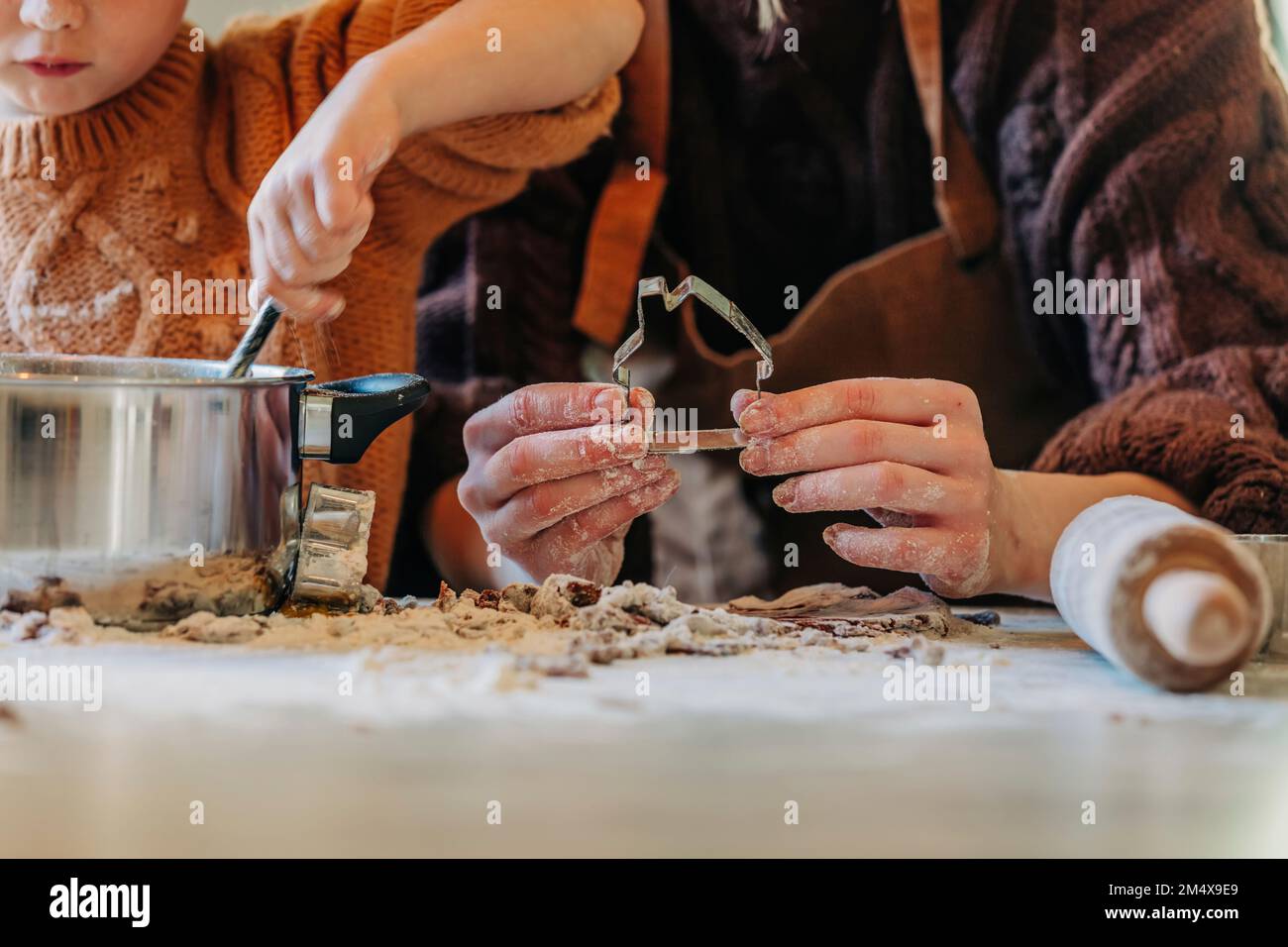 Ragazzo di cucina con madre che tiene a casa cookie cutter a tavola Foto Stock