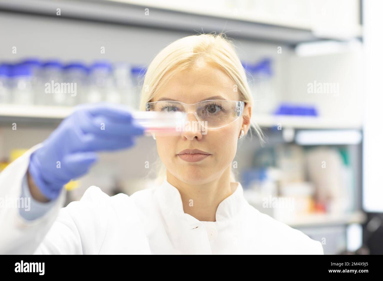 Scienziato che indossa occhiali protettivi che esamina il campione medico in laboratorio Foto Stock
