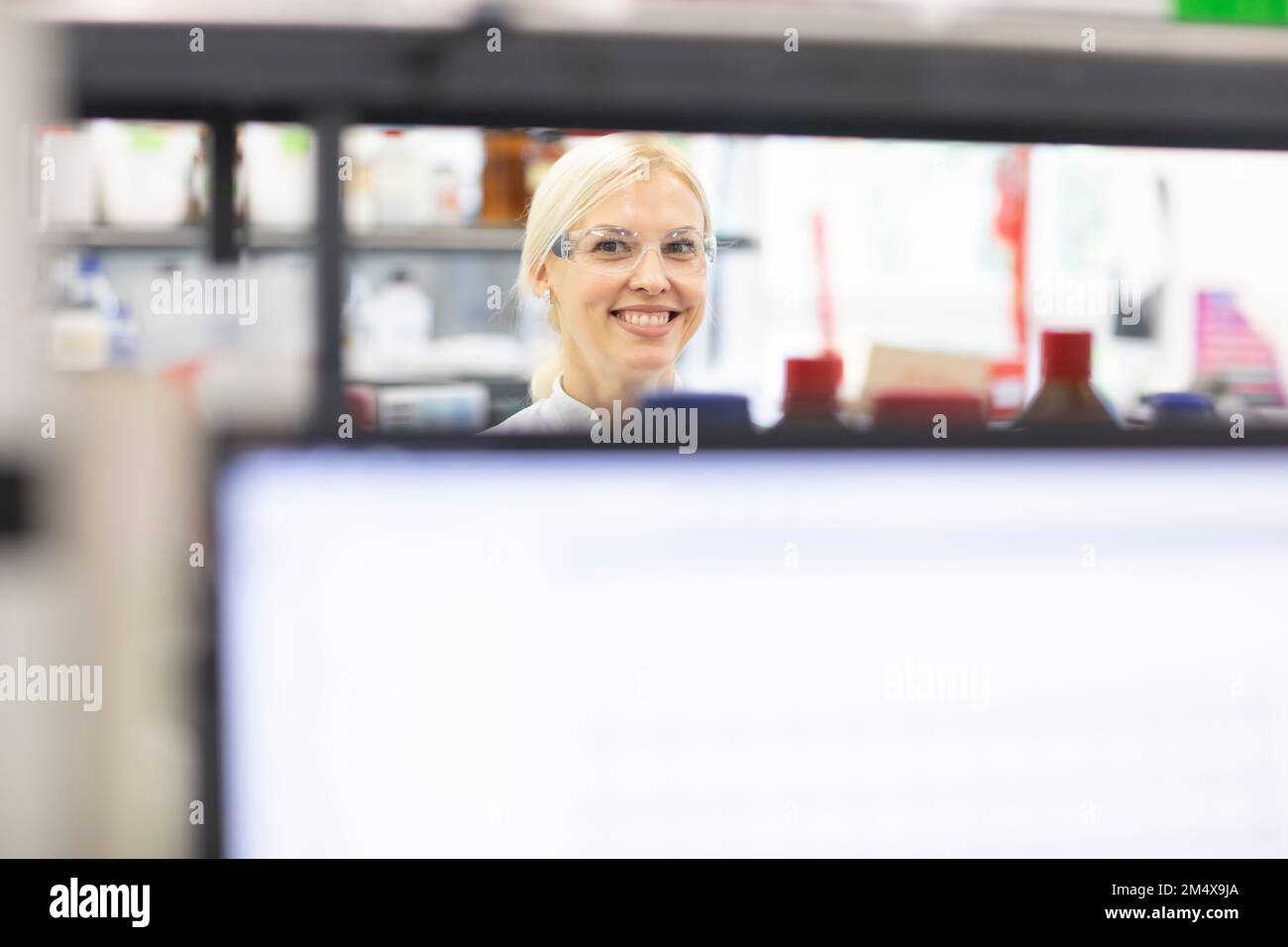Scienziato sorridente dietro lo schermo del computer al laboratorio Foto Stock