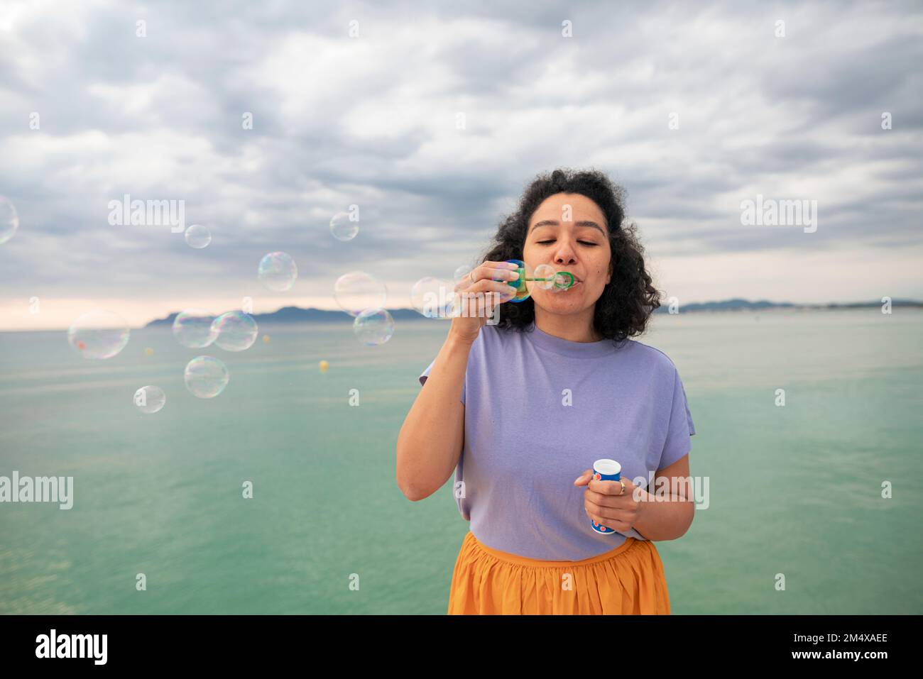 Donna che soffia bolle di fronte al mare Foto Stock