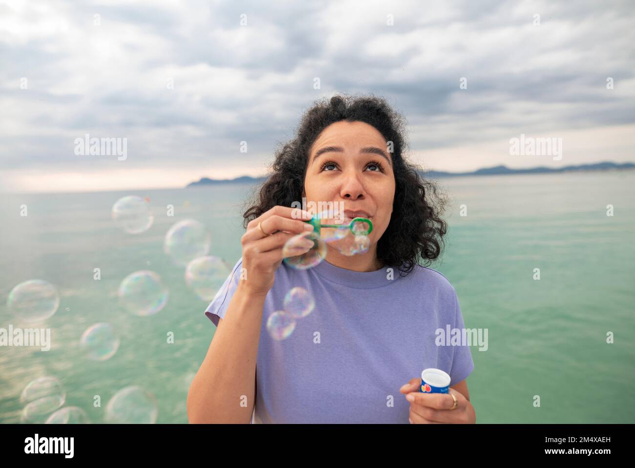 Donna che si gode bolle soffiare in piedi di fronte al mare Foto Stock