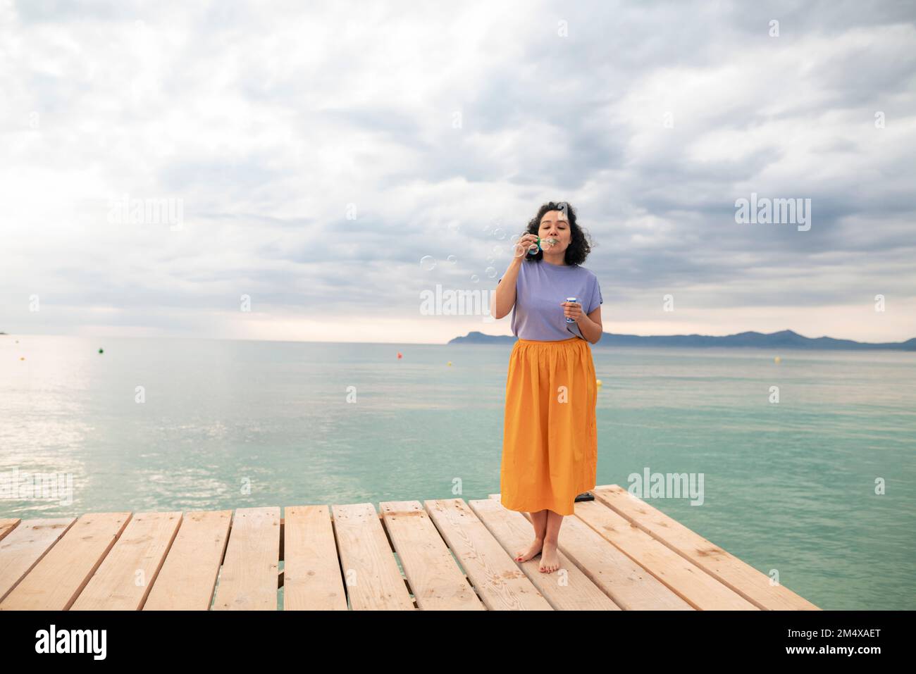 Donna in piedi sul molo che soffia bolle di fronte al mare Foto Stock