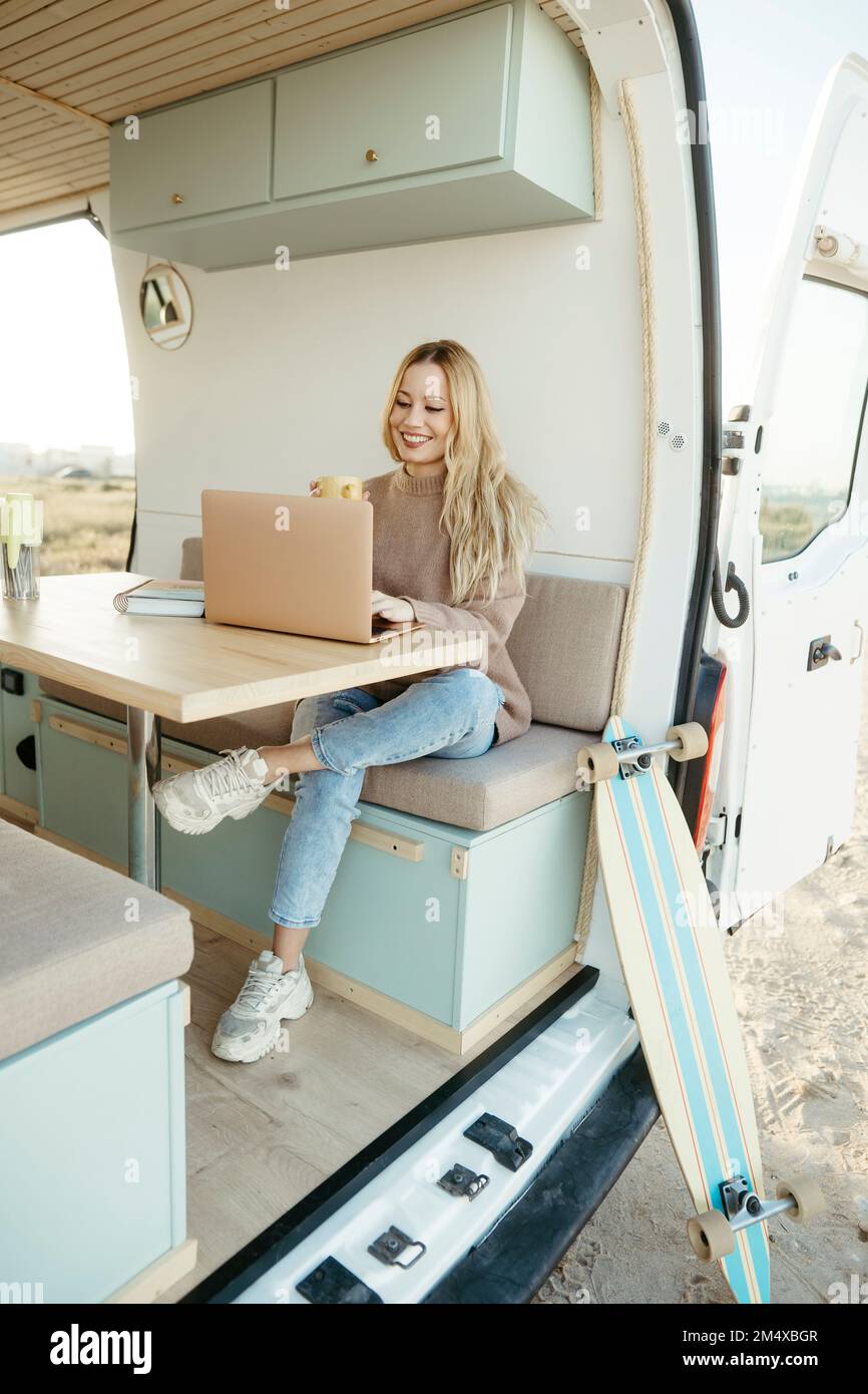 Felice nomade digitale che lavora su un notebook seduto all'interno della casa automobilistica Foto Stock