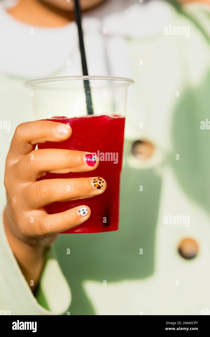 Mano di ragazza con unghie dipinte che tengono granita fragola Foto Stock